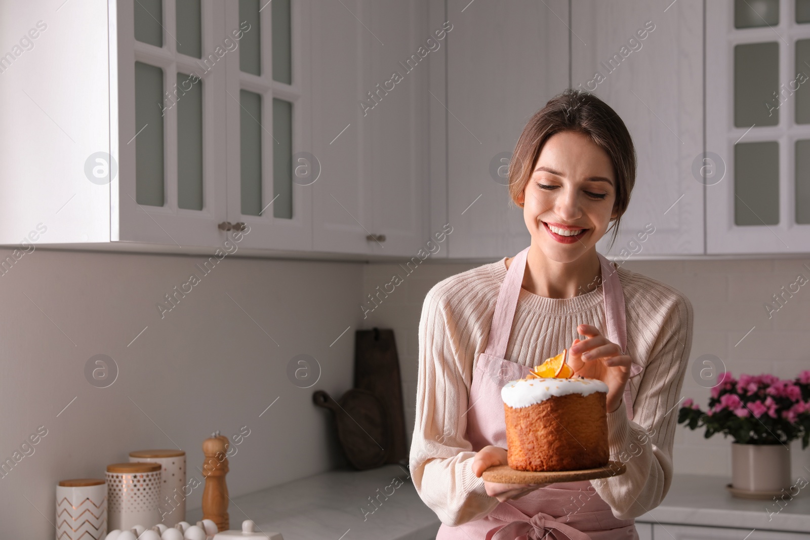 Photo of Young woman with traditional decorated Easter cake in kitchen, space for text