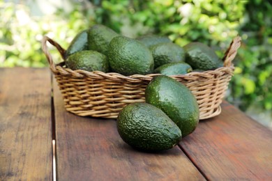 Photo of Wicker basket with fresh ripe avocados on wooden table outdoors