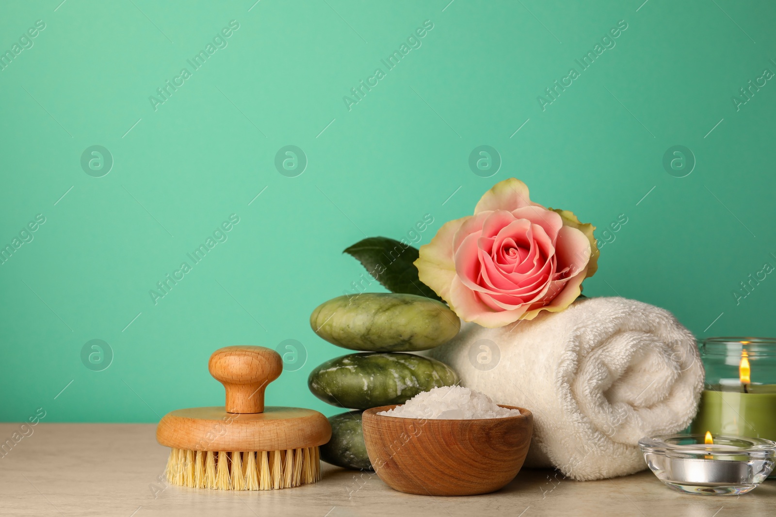 Photo of Composition with different spa products, candles and rose on beige table against turquoise background. Space for text