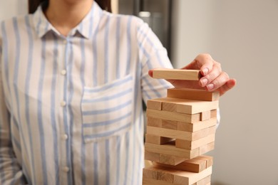 Photo of Playing Jenga. Woman building tower with wooden blocks indoors, closeup