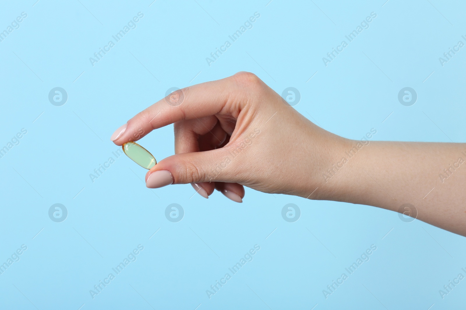 Photo of Woman holding vitamin capsule on light blue background, closeup. Health supplement