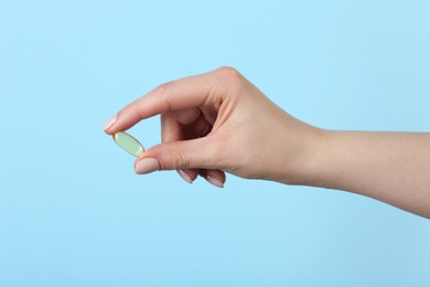 Photo of Woman holding vitamin capsule on light blue background, closeup. Health supplement