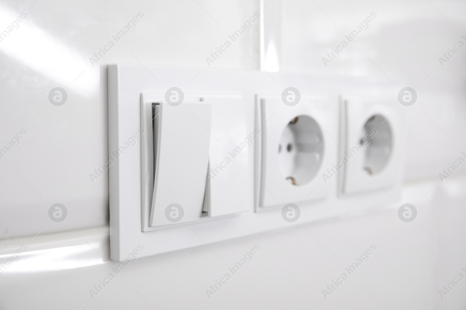 Photo of Light switch and power sockets on white wall indoors, closeup