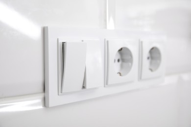Light switch and power sockets on white wall indoors, closeup