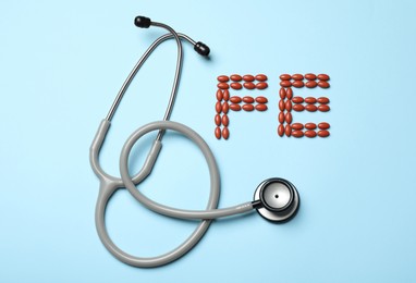 Photo of Pills and stethoscope on light blue background, flat lay. Anemia concept