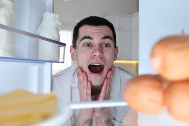 Photo of Surprised man near refrigerator in kitchen, view from inside