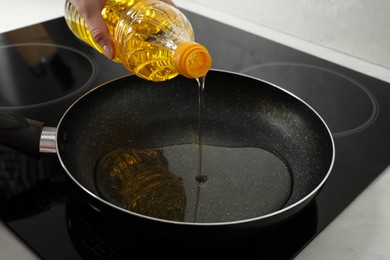 Photo of Woman pouring cooking oil into frying pan on stove, closeup