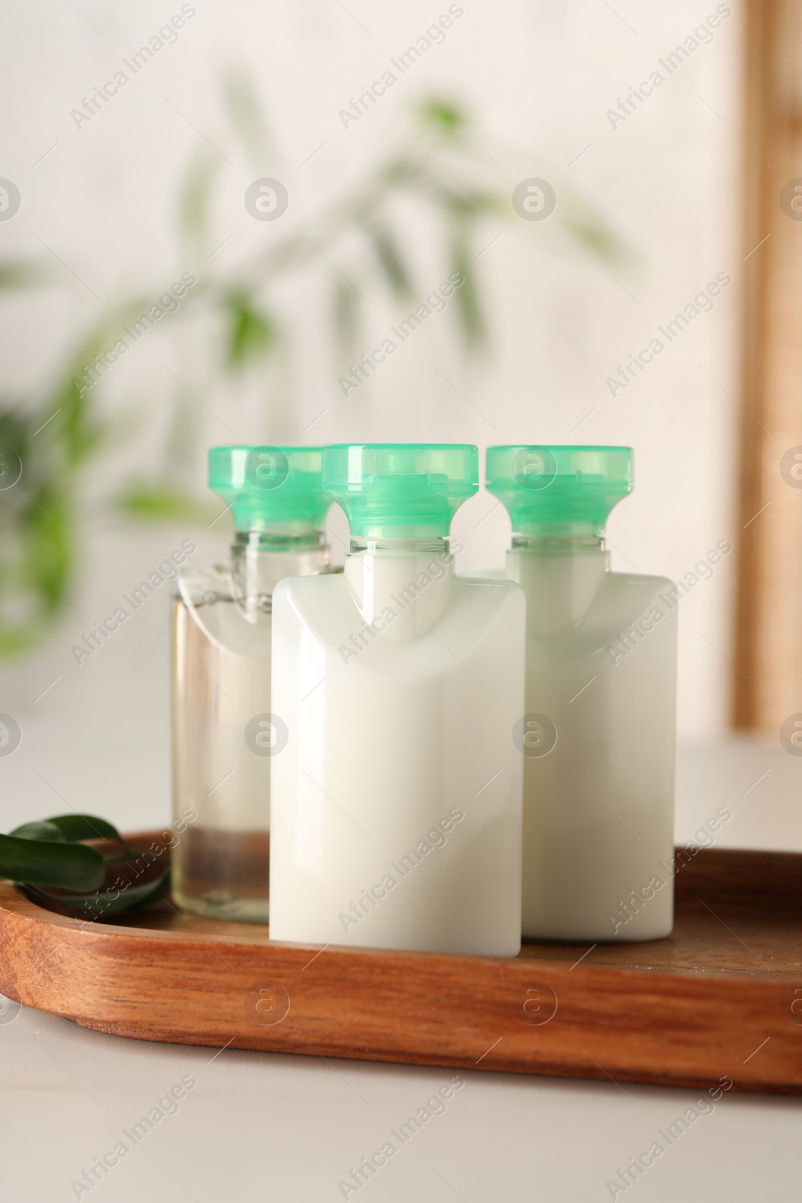 Photo of Mini bottles of cosmetic products on white table against blurred background