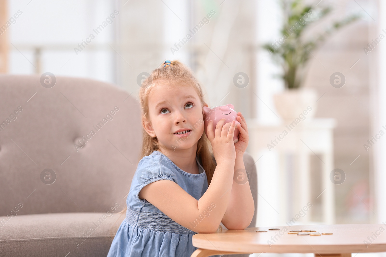 Photo of Little girl with piggy bank and money at home