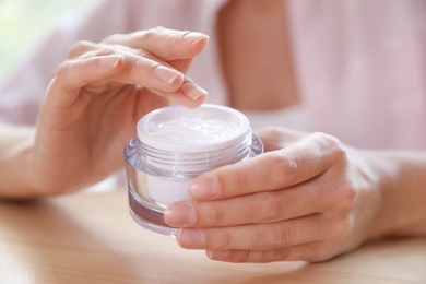 Photo of Woman with jar of moisturizing cream at table, closeup