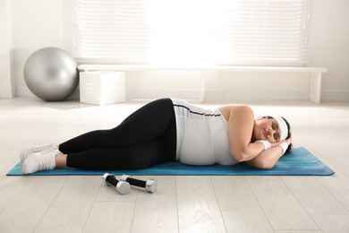 Photo of Lazy overweight woman sleeping instead of training on mat at gym