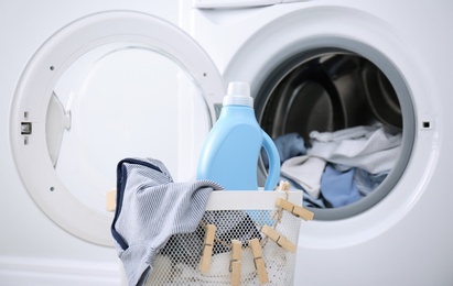 Photo of Bottle of detergent and children's clothes in basket near washing machine