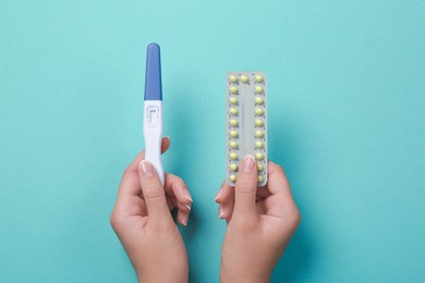 Photo of Woman holding birth control pills pregnancy test on light blue, top view closeup