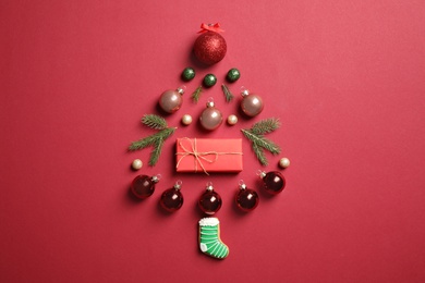 Photo of Christmas tree silhouette of fir branches and festive decoration on red background, flat lay