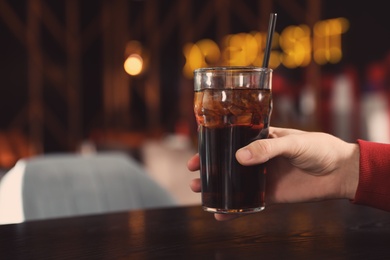 Photo of Man holding glass of refreshing cola at table indoors, closeup. Space for text