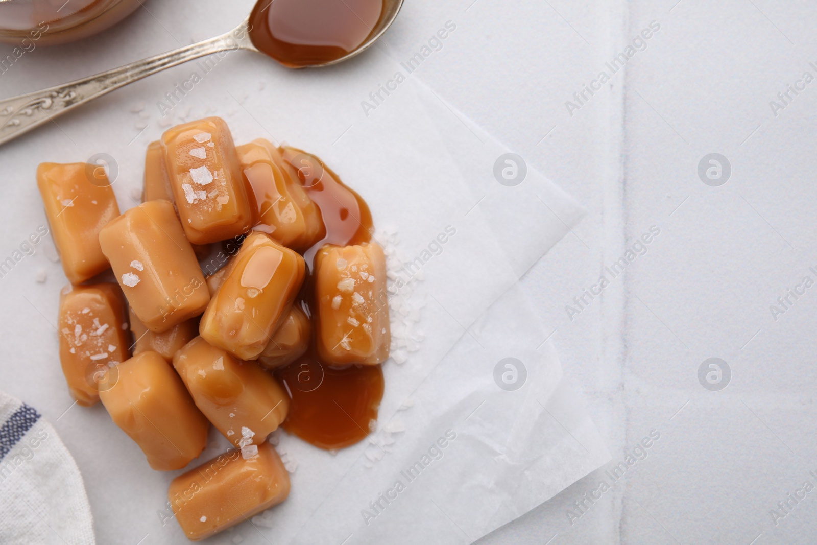 Photo of Yummy caramel candies and sea salt on white table, flat lay. Space for text