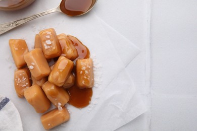 Yummy caramel candies and sea salt on white table, flat lay. Space for text