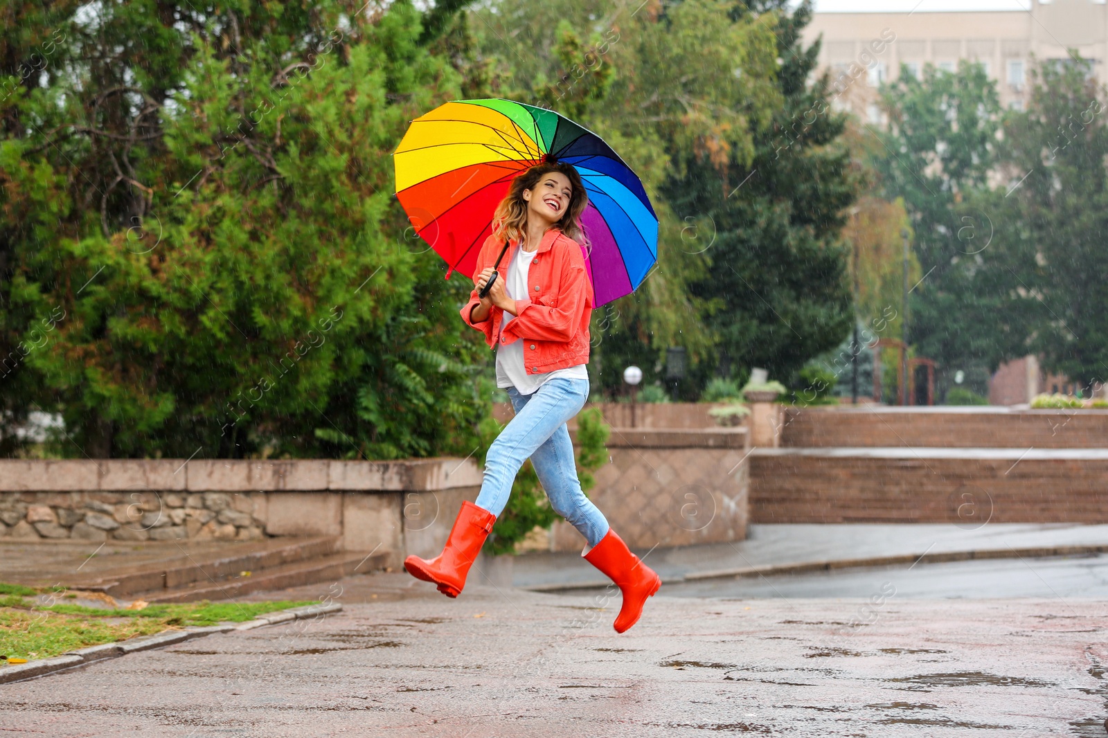 Photo of Happy young woman with bright umbrella under rain outdoors