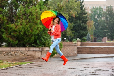 Photo of Happy young woman with bright umbrella under rain outdoors