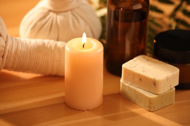 Photo of Spa composition. Cosmetic products, herbal bags and burning candle on wooden table, closeup