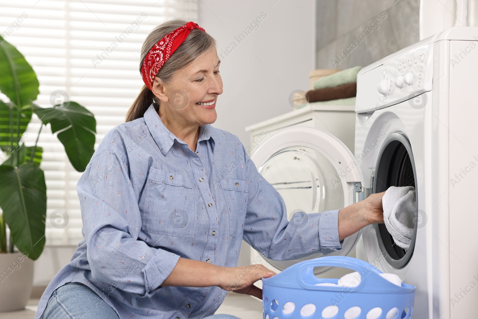 Photo of Happy housewife putting laundry into washing machine at home