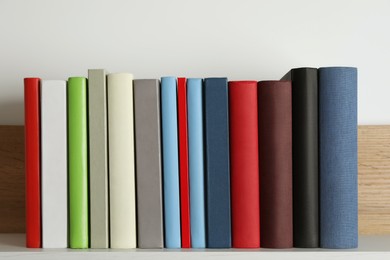 Many hardcover books on wooden shelf near white wall