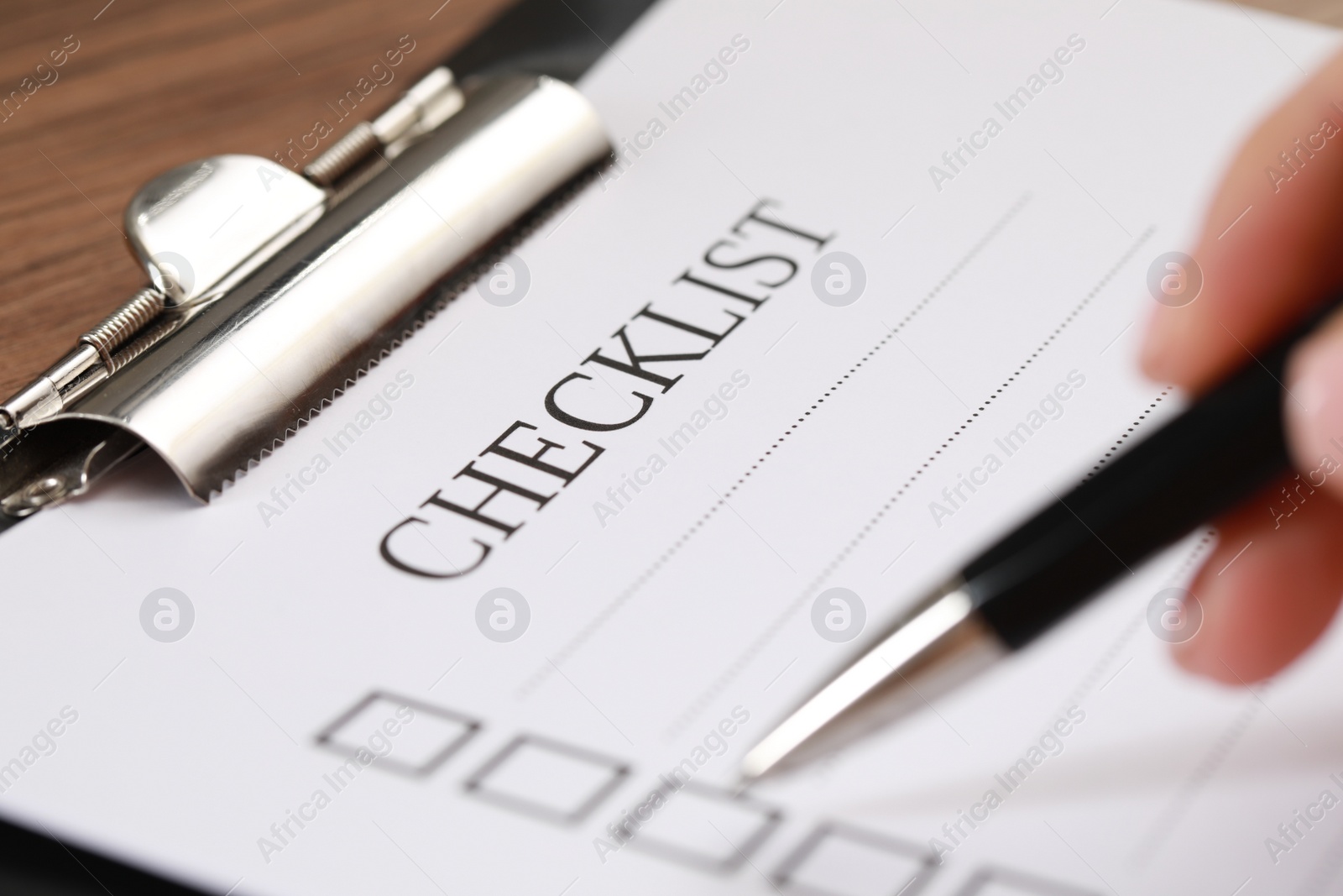 Photo of Woman filling Checklist at wooden table, closeup