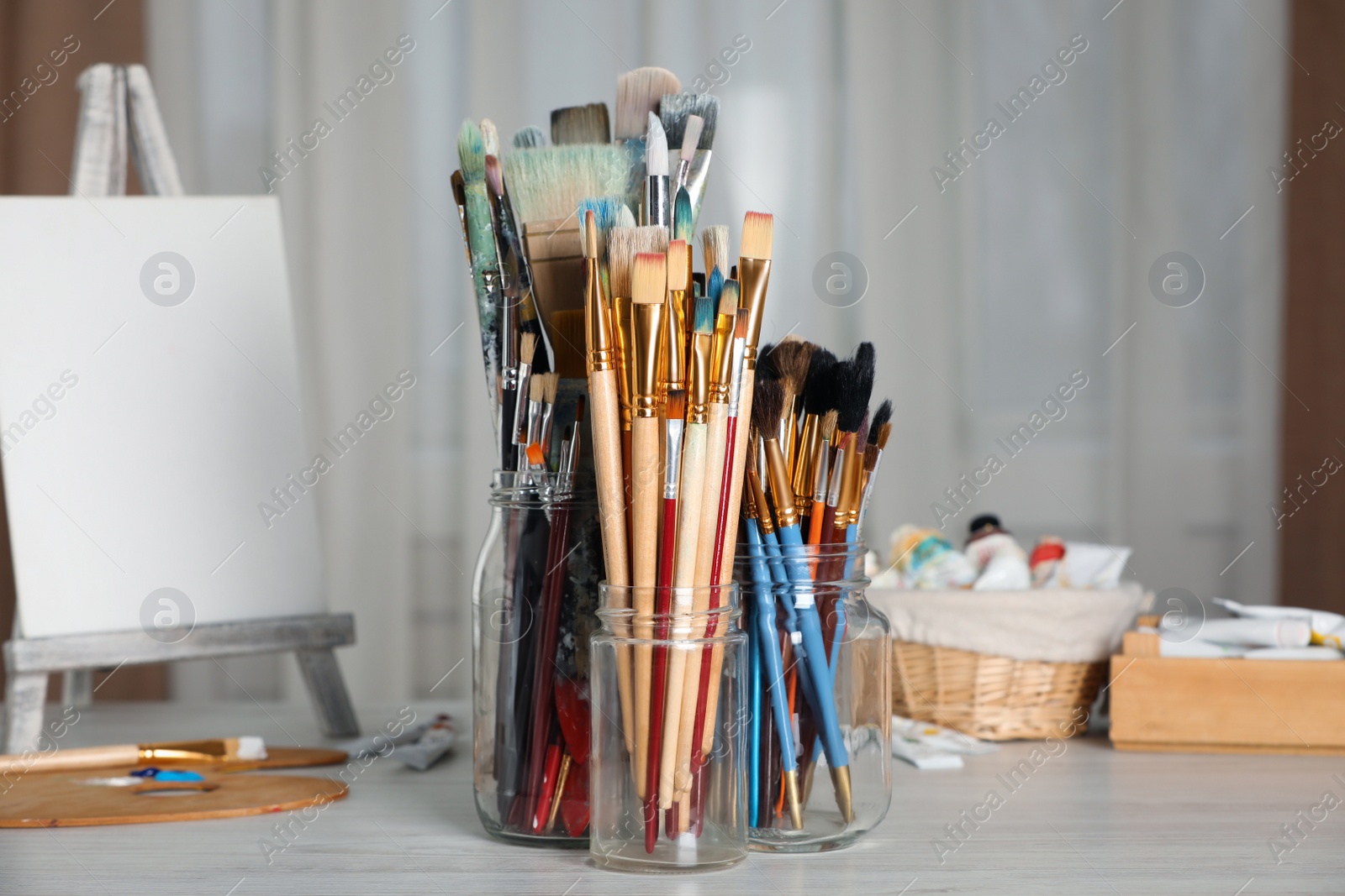 Photo of Glass jars with many different paintbrushes on white wooden table indoors