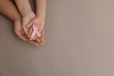 Family holding pink ribbon on grey background, top view with space for text. Breast cancer awareness