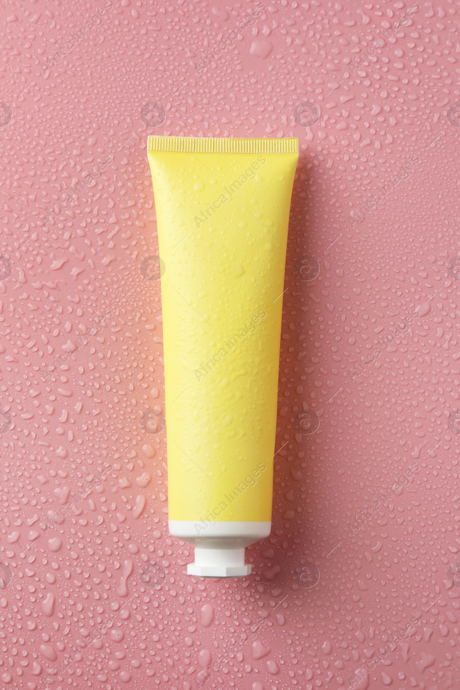 Photo of Moisturizing cream in tube on pink background with water drops, top view