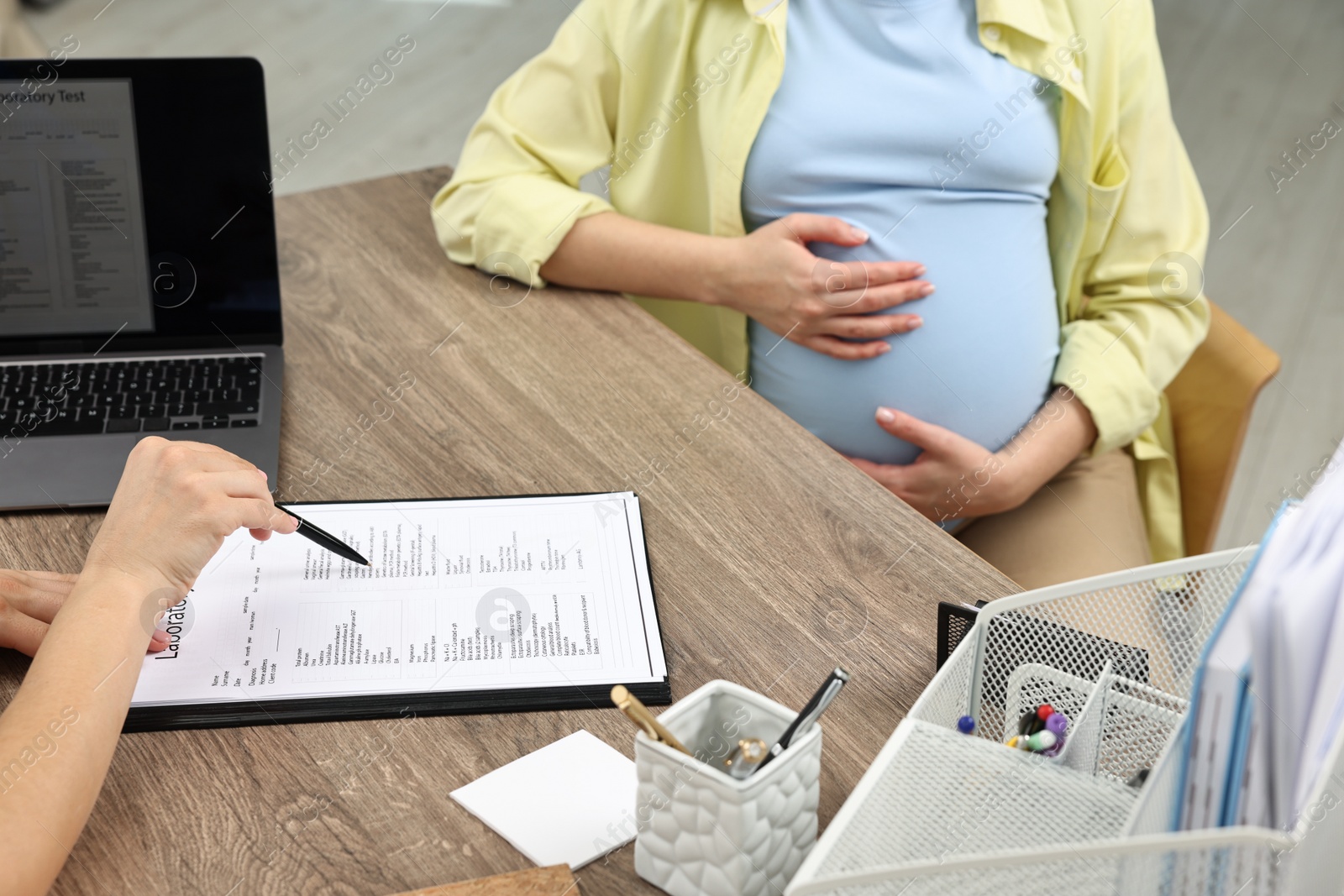 Photo of Doctor showing results of laboratory test to pregnant patient at table in clinic, closeup