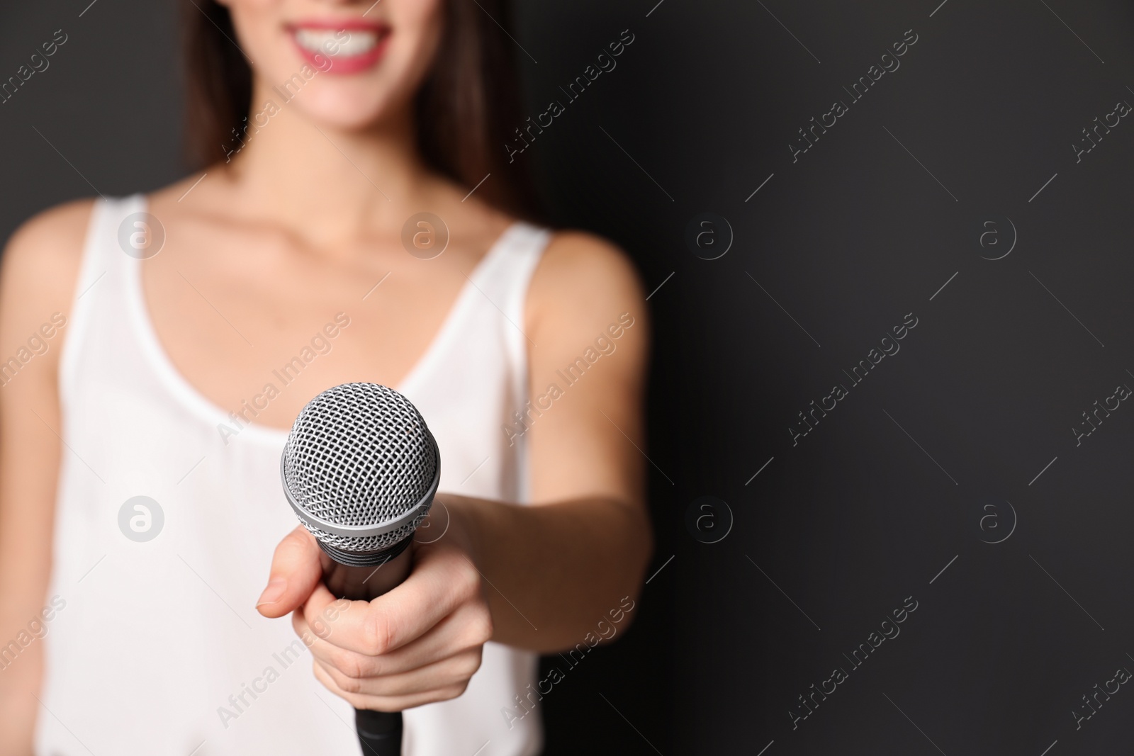 Photo of Young woman holding microphone on dark background, closeup view with space for text