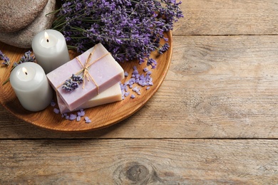 Photo of Burning candles, stones, soap bars and lavender flowers on wooden table. Space for text