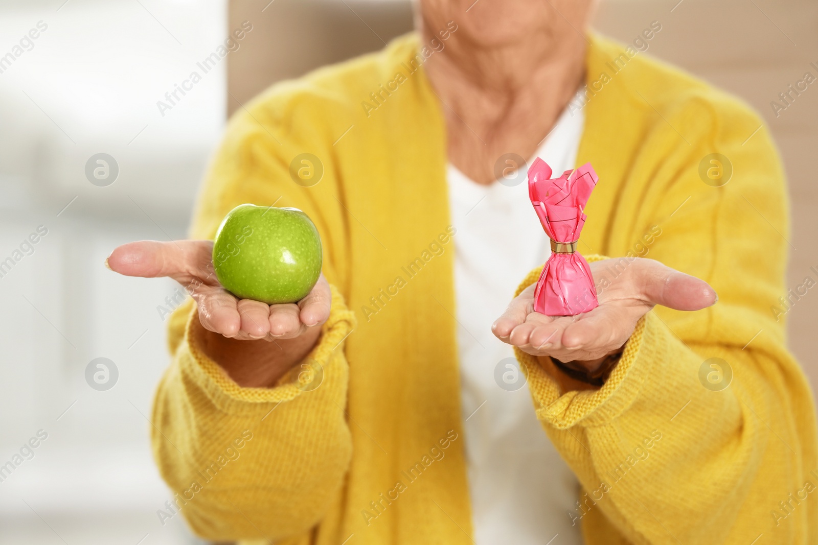 Photo of Senior woman with between apple and candy in hospital, closeup. Diabetes diet