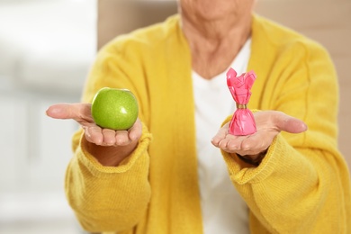 Photo of Senior woman with between apple and candy in hospital, closeup. Diabetes diet