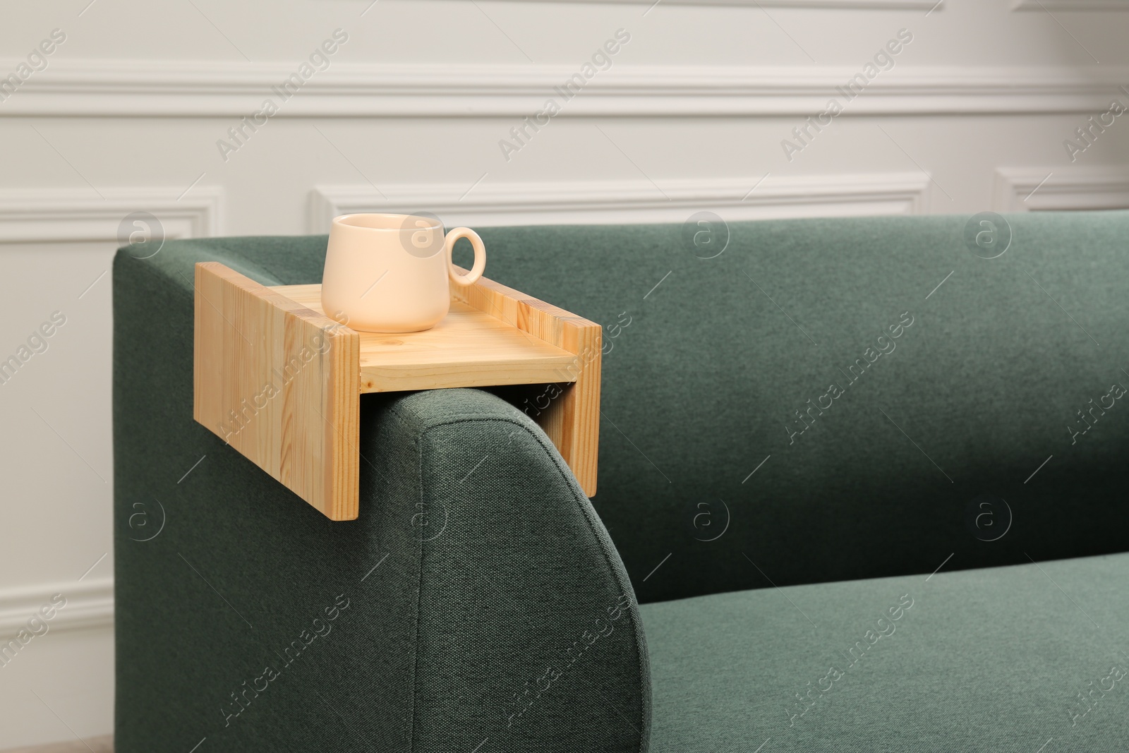 Photo of Cup of tea on sofa with wooden armrest table in room, space for text. Interior element