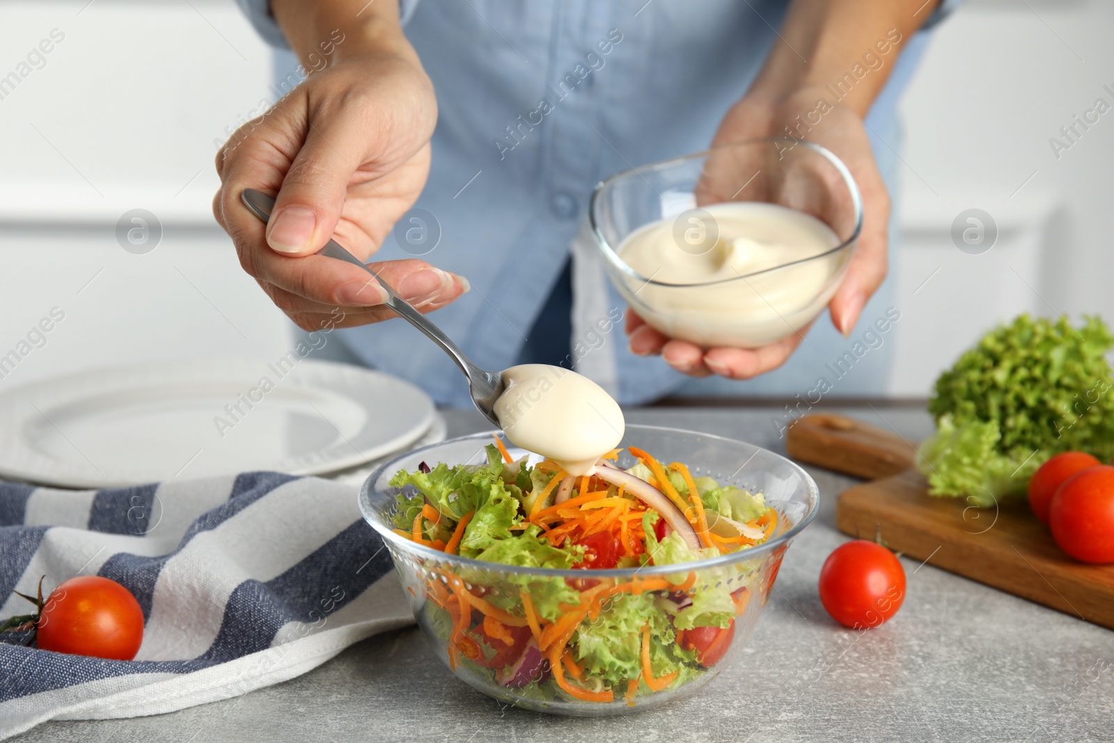 Photo of Woman adding mayonnaise to delicious salad at grey table, closeup