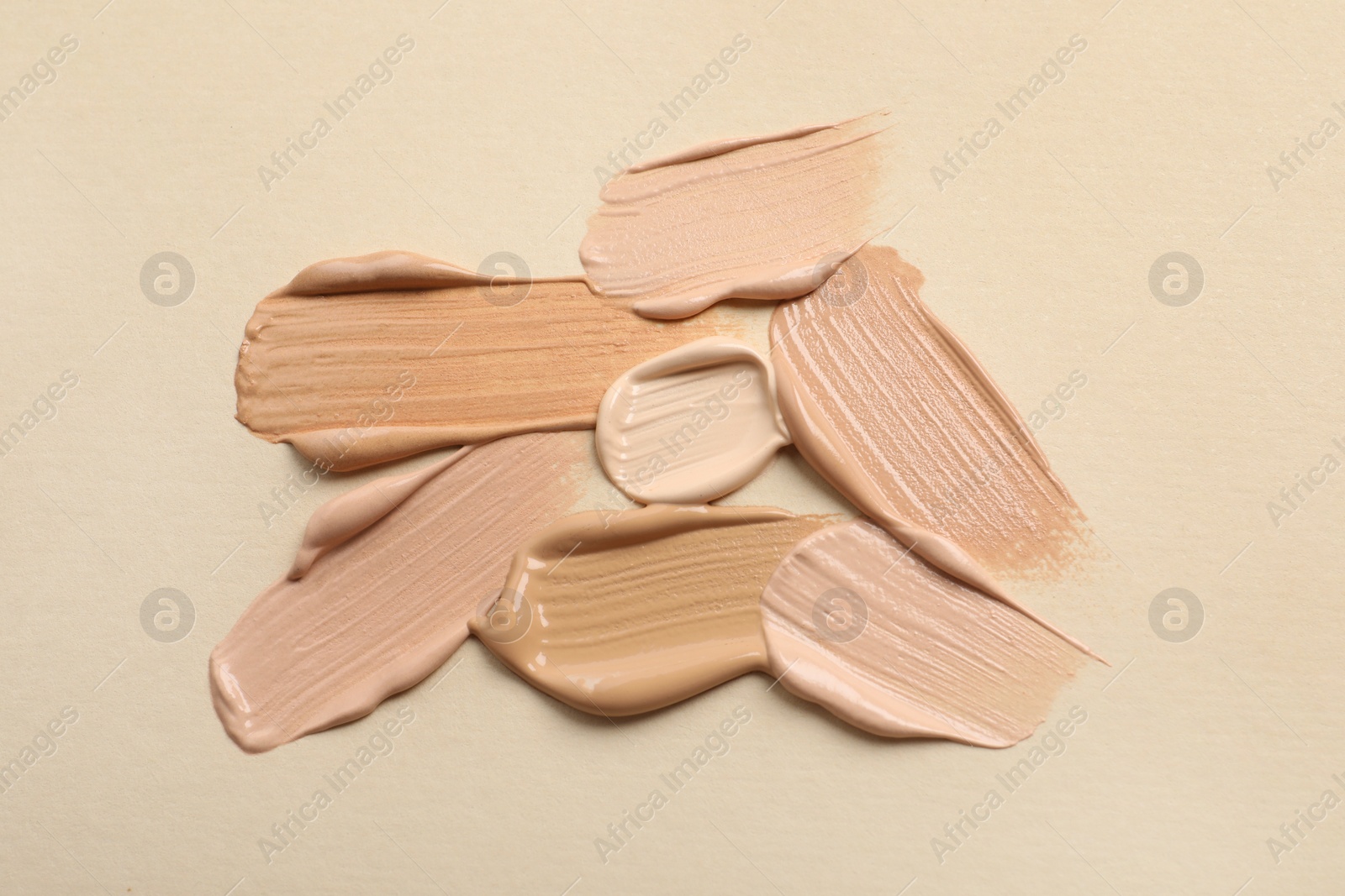 Photo of Samples of skin foundation on beige background, top view