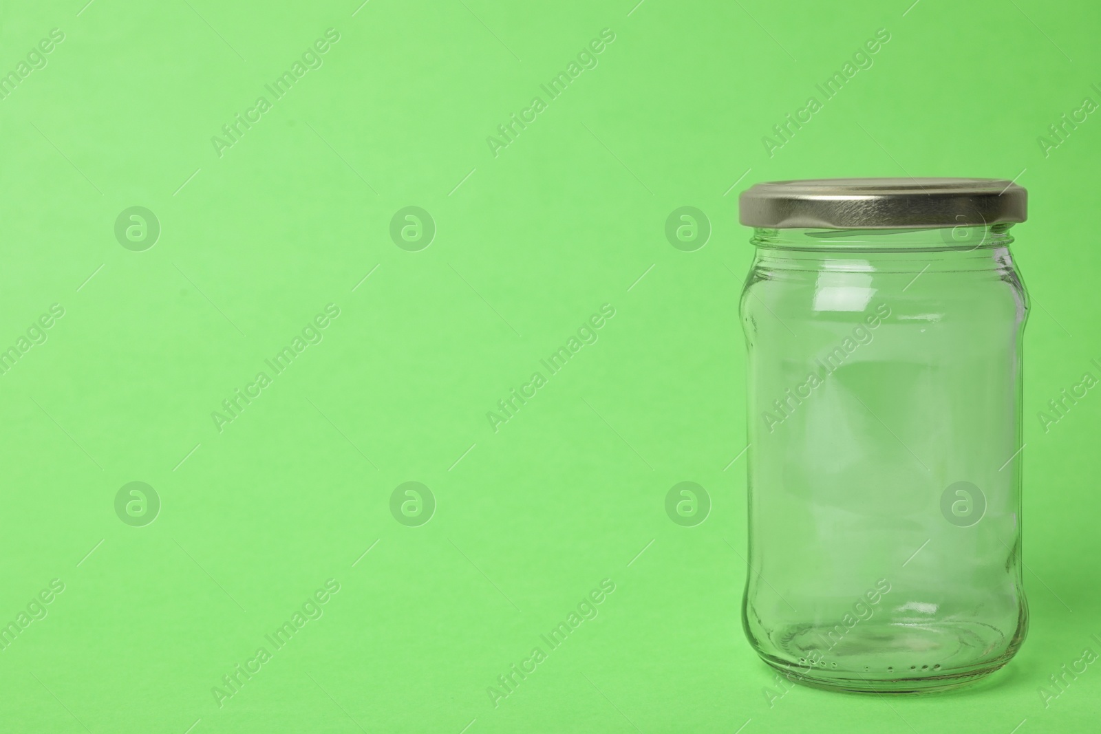 Photo of Closed empty glass jar on light green background, space for text