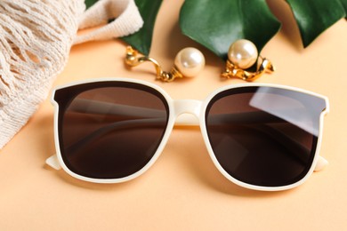 Photo of New stylish elegant sunglasses and beautiful earrings on beige background, closeup
