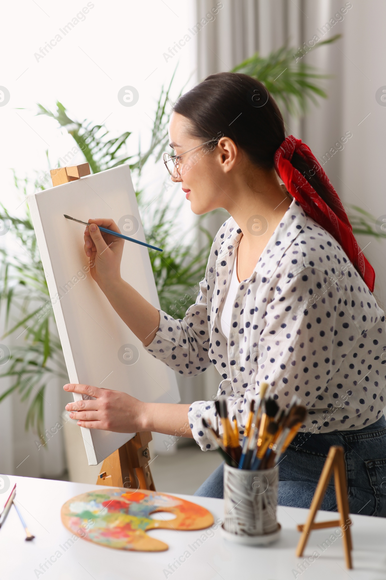 Photo of Happy woman artist drawing picture on canvas indoors