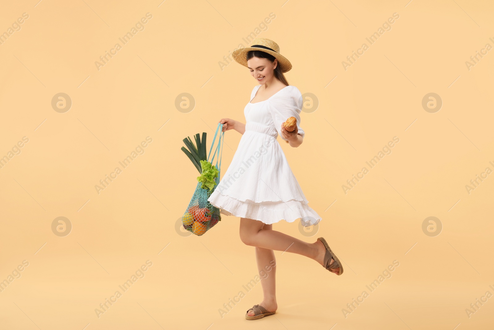 Photo of Woman with string bag of fresh vegetables and baguette on beige background