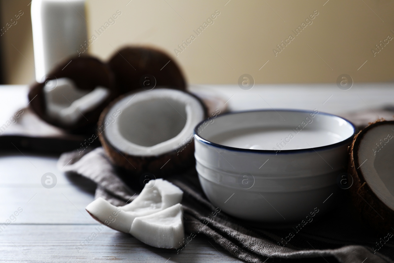 Photo of Bowl of coconut milk and nuts on white wooden table, space for text