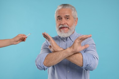 Photo of Stop smoking concept. Senior man refusing cigarette on light blue background