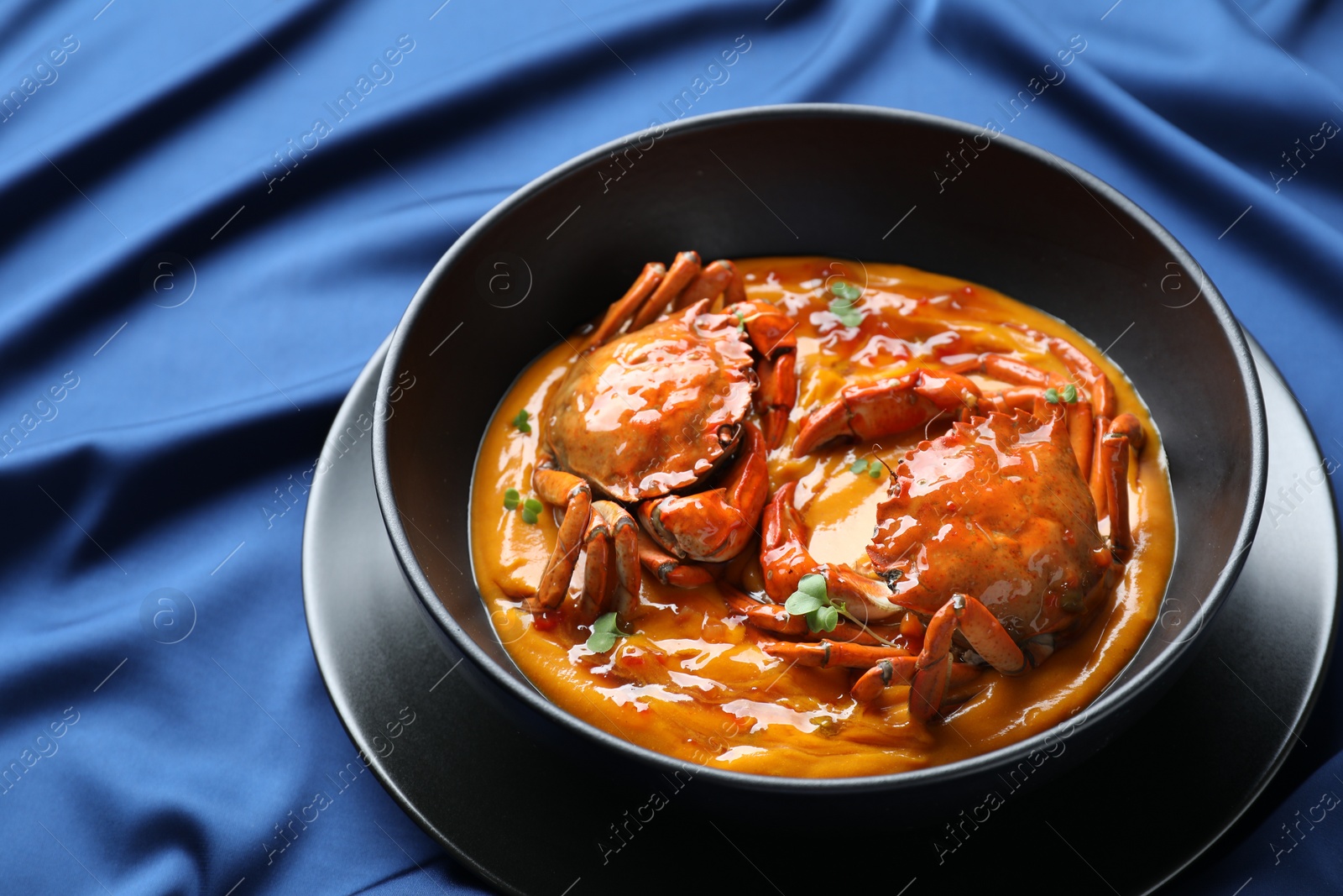 Photo of Delicious boiled crabs with sauce in bowl on blue tablecloth. Space for text