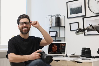 Professional photographer in glasses holding digital camera at table in office