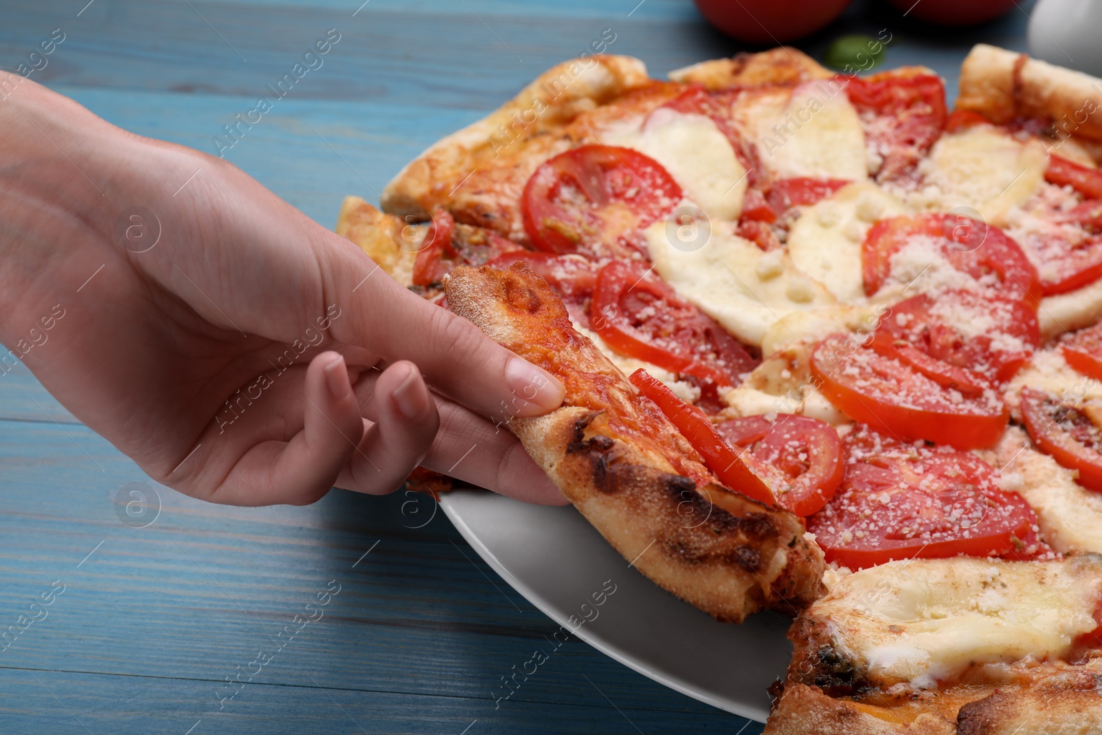 Photo of Woman taking piece of delicious Caprese pizza at blue wooden table, closeup