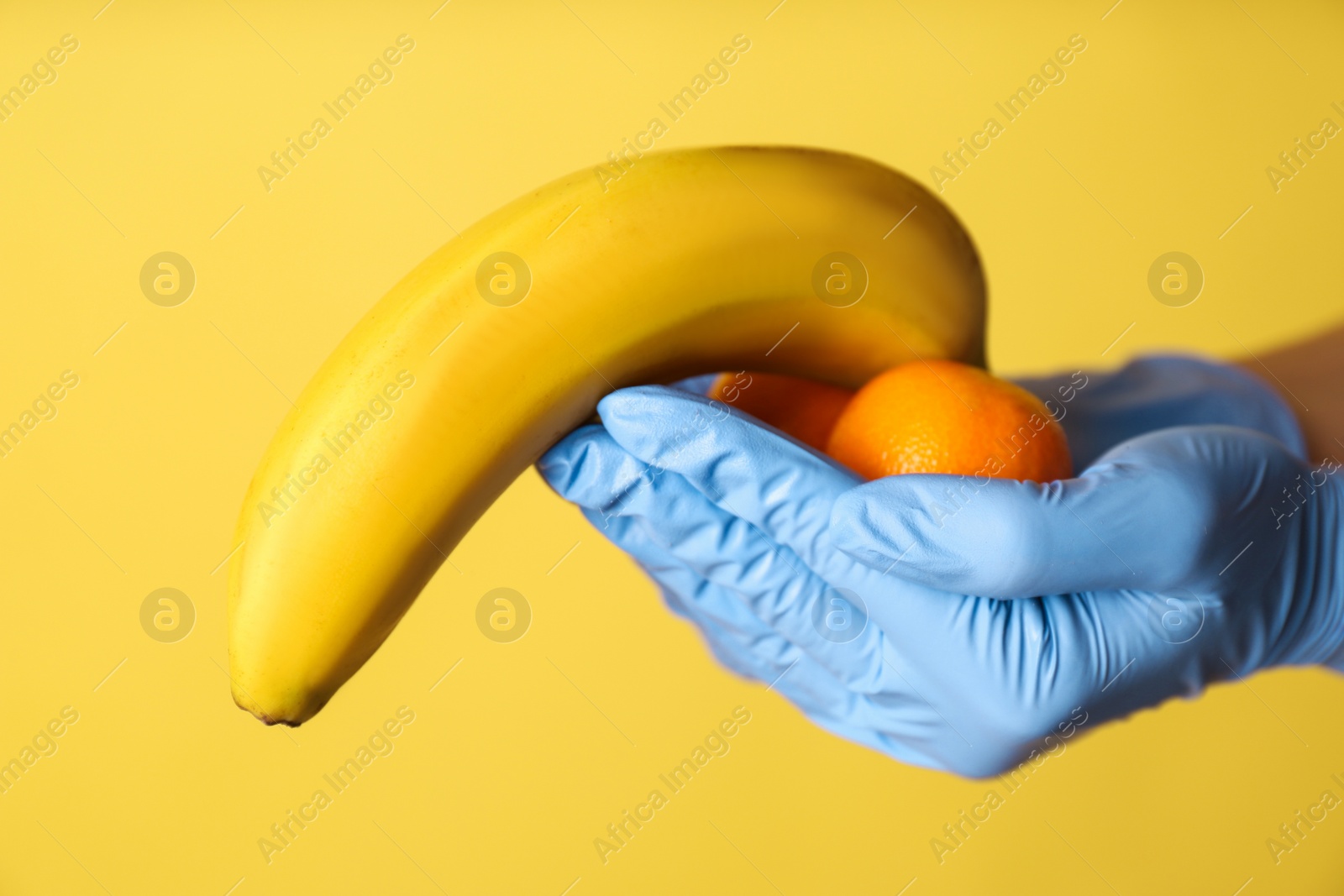 Photo of Doctor holding fruits symbolizing male sexual organ on yellow background, closeup. Potency problem