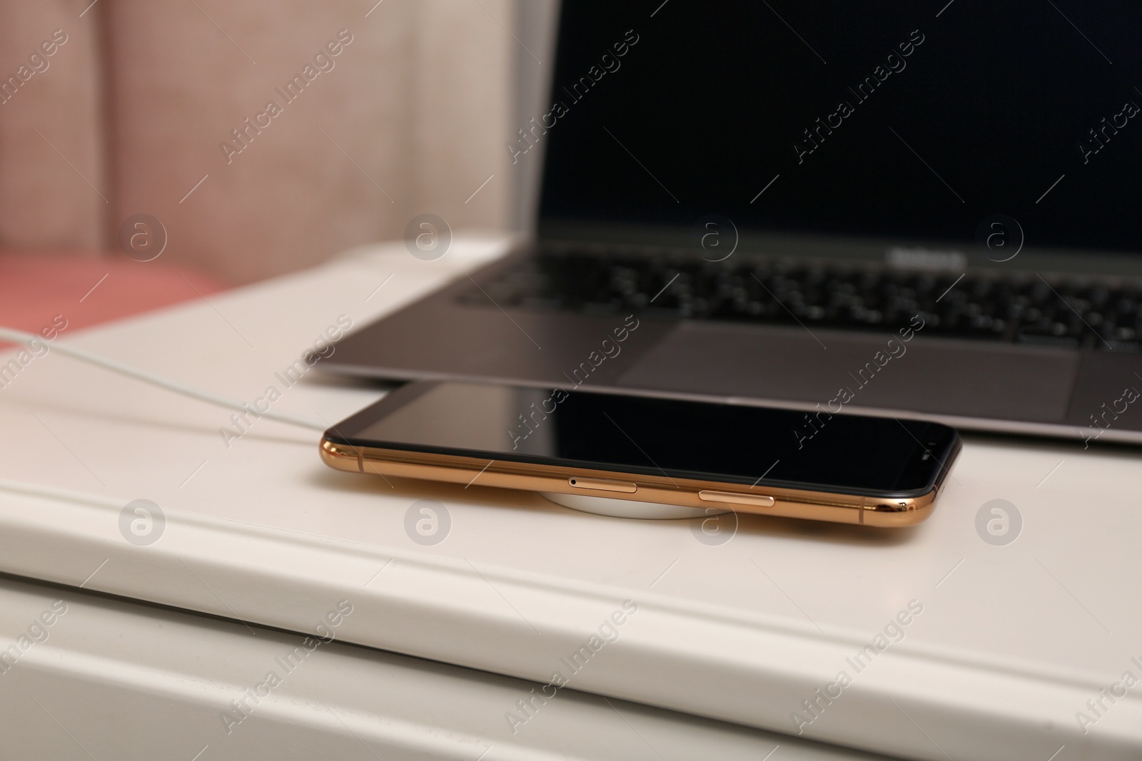 Photo of Smartphone with wireless charger connected to laptop on white table, closeup