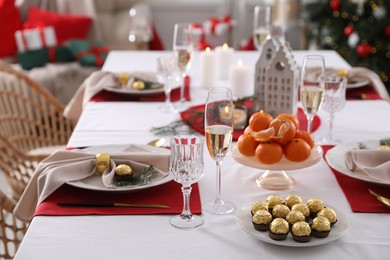 Christmas table setting with tangerines, candies and dishware indoors